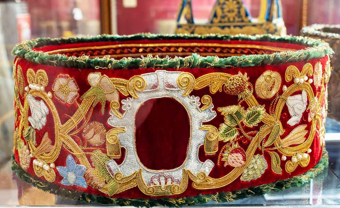 Photo of a crown with scrolls in gold threads and flowers in coloured metal threads.