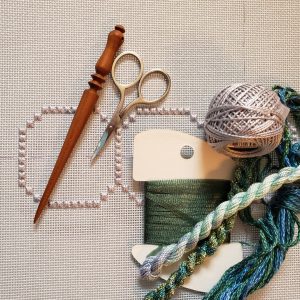 photo of a piece of embroidery canvas with a laying tool, small scissors, and a variety of threads