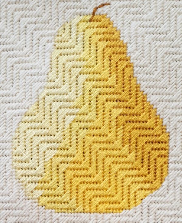 A photo of an embroidered, textured pear on a textured background. The pear is stitched in shades of yellow to give it a rounded appearance.