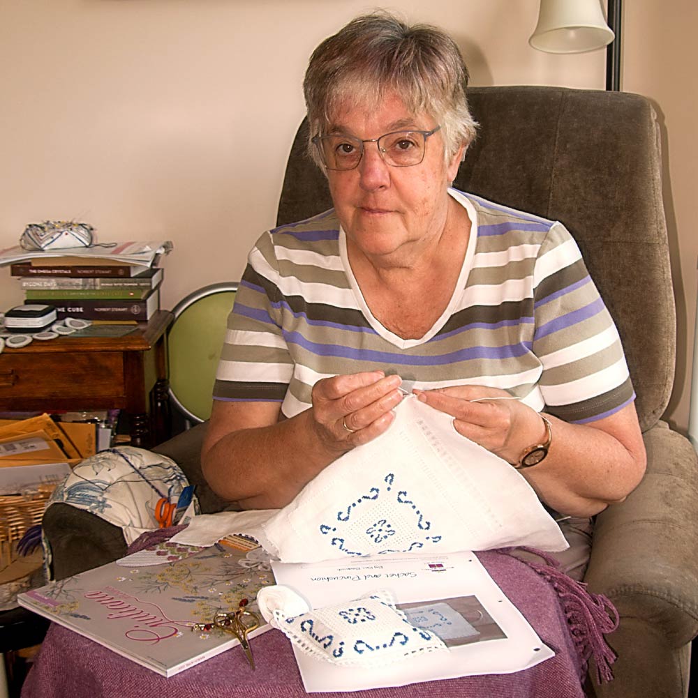 photo a woman in a comfortable chair embroidering a blue design on a white piece of fabric