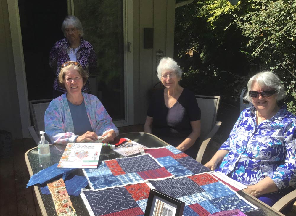 photo of a group of four women outside with embroidery on the table in front of them and a copy of Giuliana Ricama magazine.