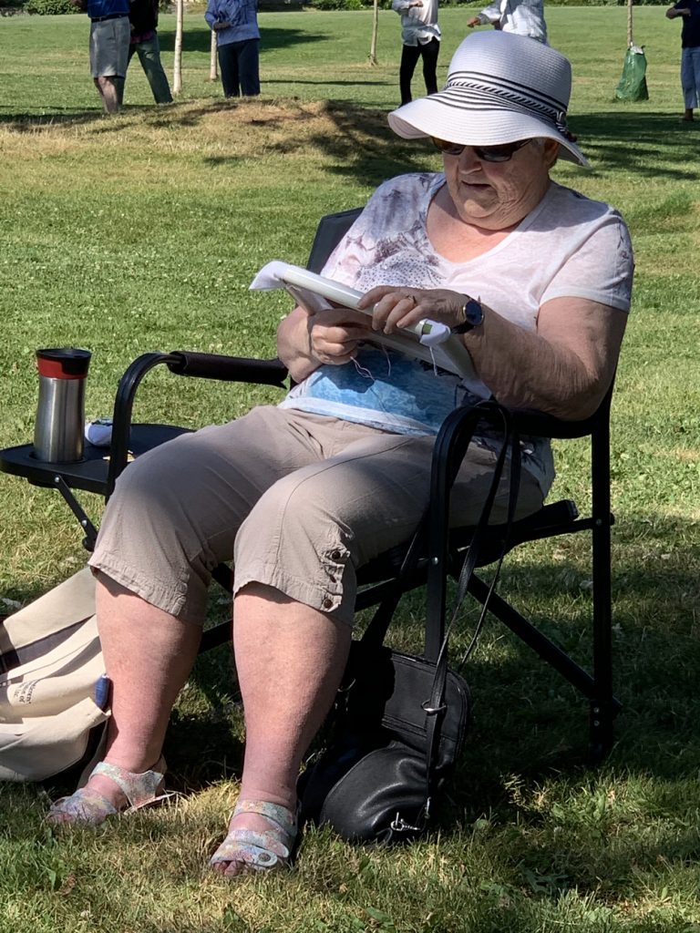 photo of a woman in a lawn chair doing embroidery outside in the shade