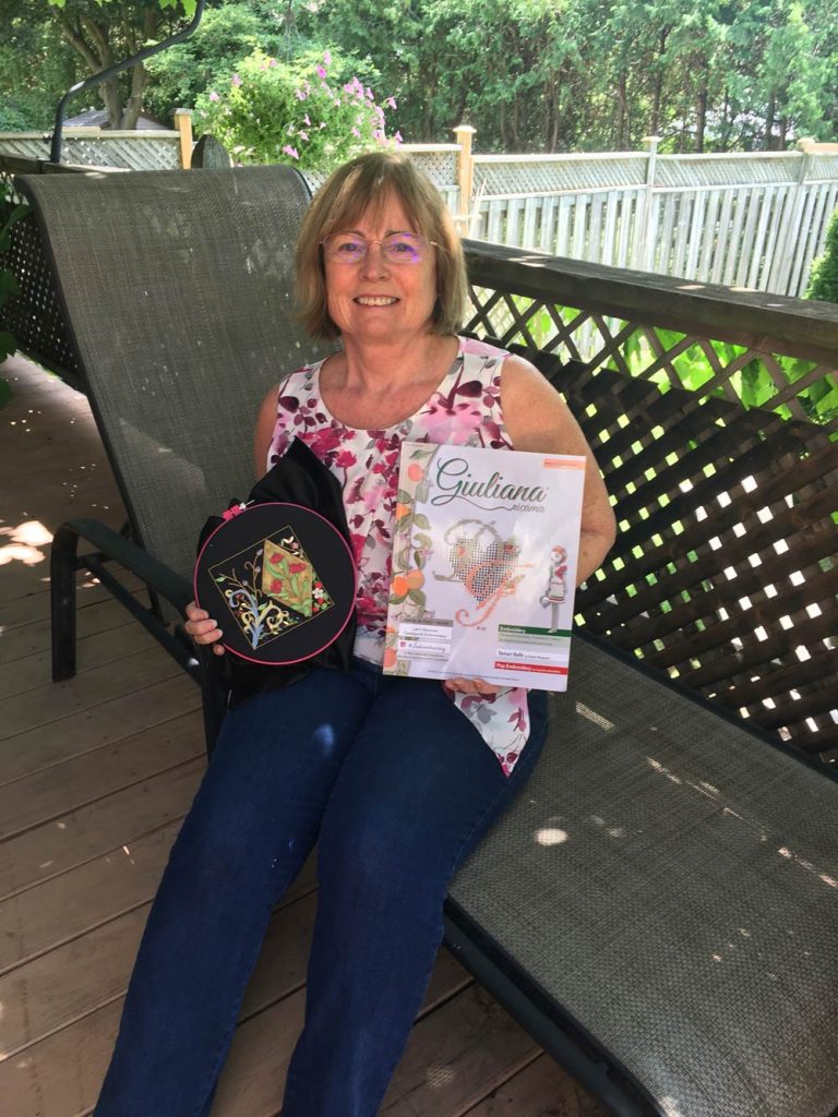 phot of a woman sitting on a outdoor deack holding a piece of embroidery and Giuliana Ricama magazine.