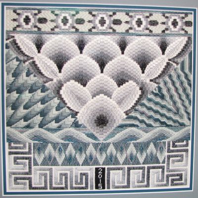 Canvas work style of embroidery in grey threads with Roman key and turtle shaped borders, diamond, zigzag and clamshell shapes in the middle.