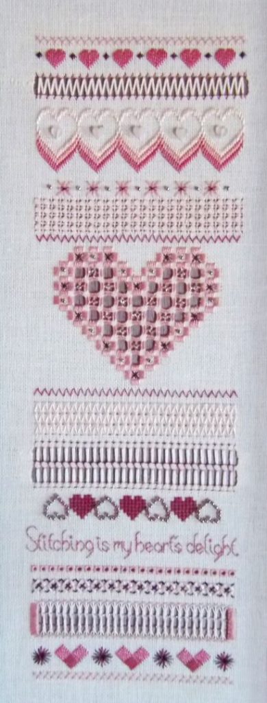 photo of a tall narrow sampler with bands of a variety of stitches, many forming heart shapes