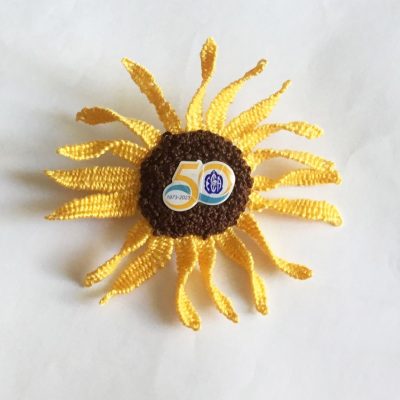 Photo of a sunflower brooch of embroidery woven petals and leave with a 50th-anniversary pin in the centre.