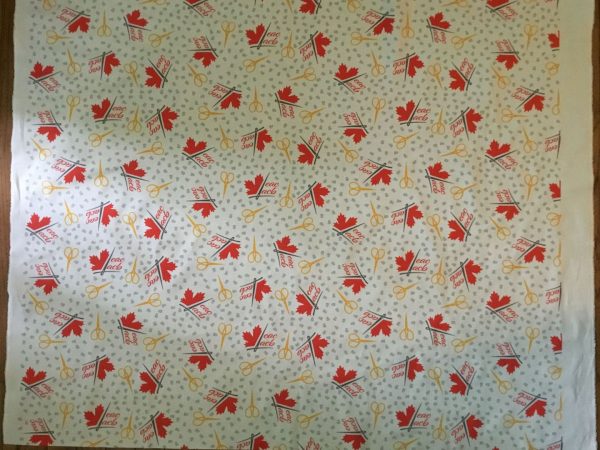 photo of a flat piece of fabric with a repeating pattern consisting of the EAC/ACB logo, thimbles and scissors