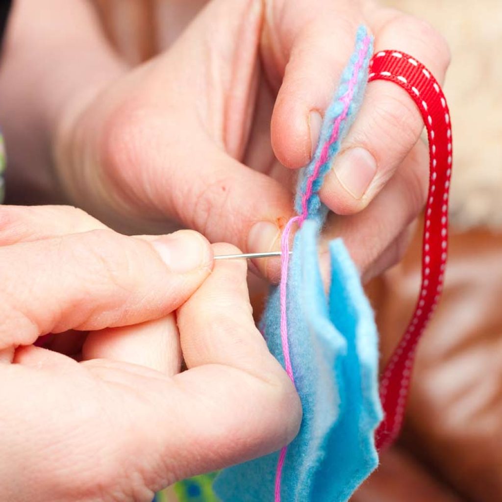 Close-up photo of hands embroidering a blanket stitch to join two pieces of felt.