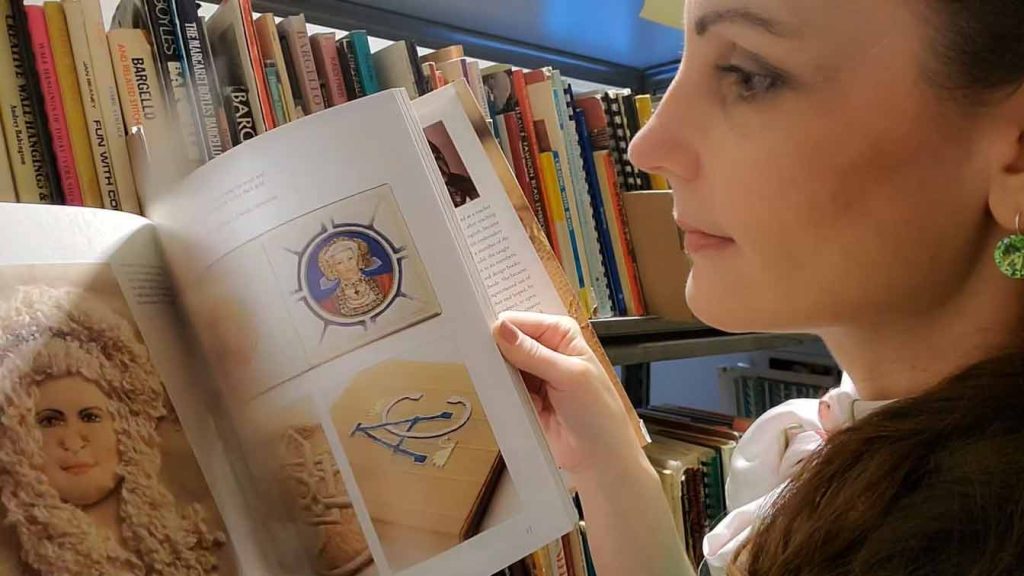 Photo of a woman flipping through a book that shows embroidered faces.