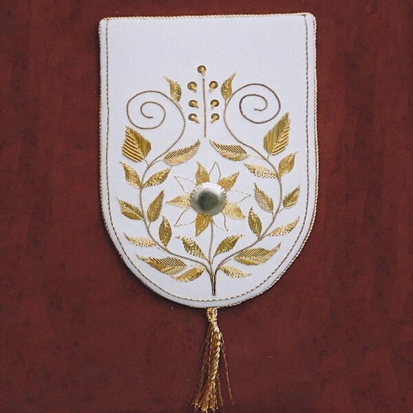 Photo of an embroidered fabric with a rounded bottom edge and a symmetrical pattern of vines and leaves stitched with gold-coloured thread.
