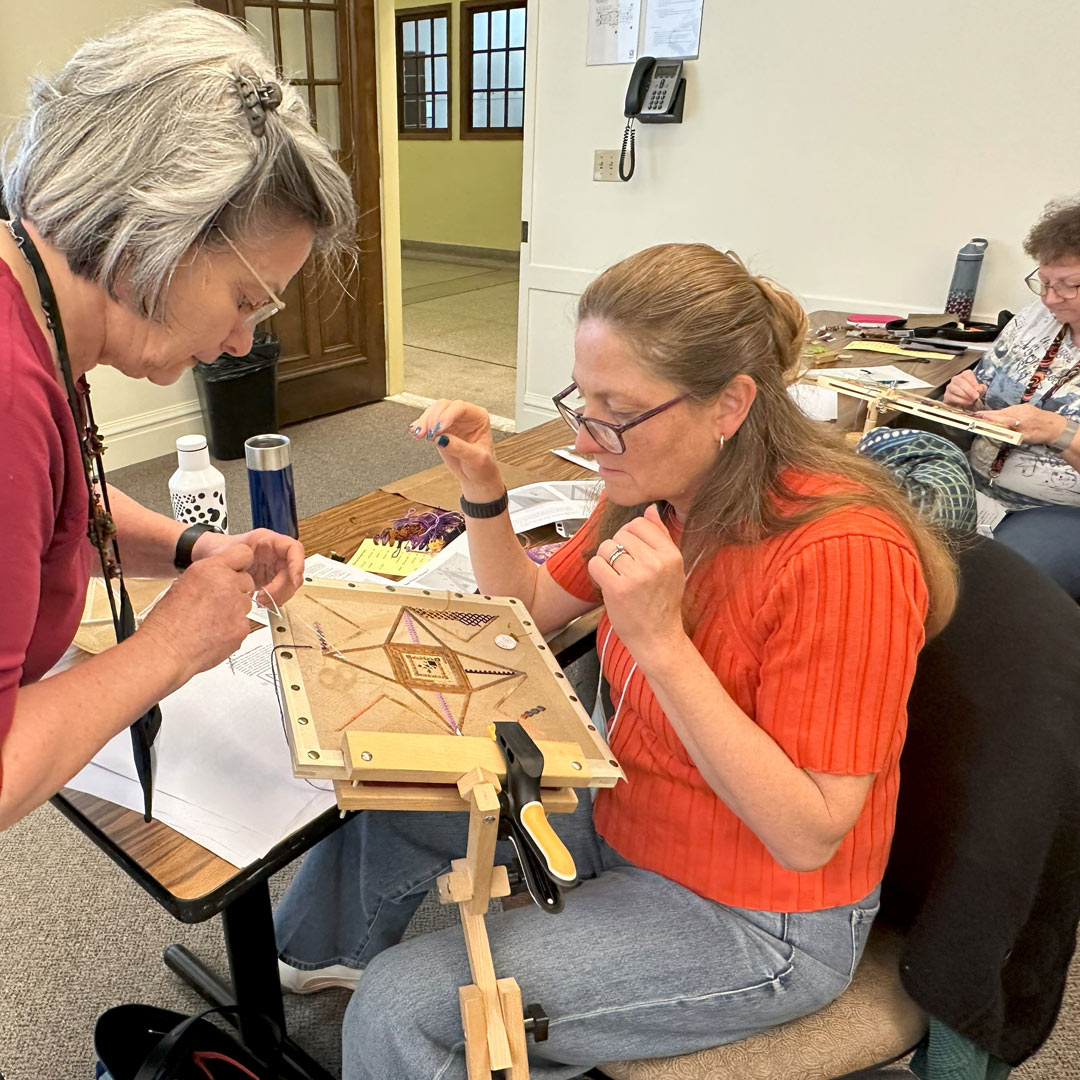photo of an embroidery instructor helping a student with their embroidery