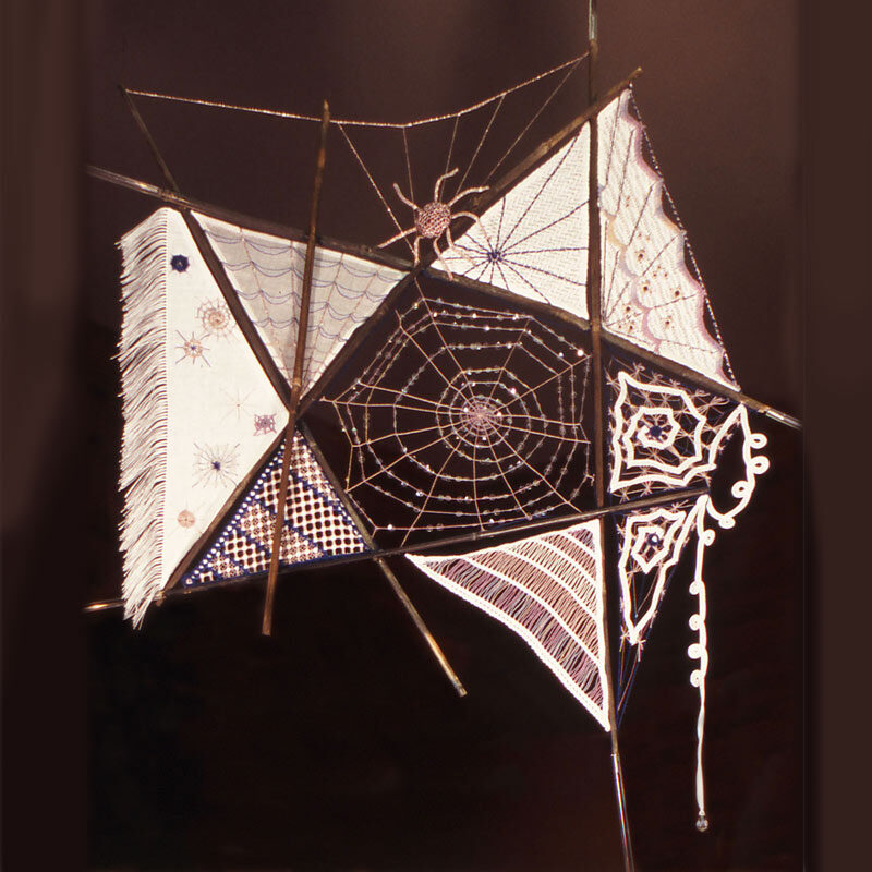 Photo of a star-shaped embroidery of a spider's web with various embroidery pieces filling some of the shapes, and extending beyond the star.