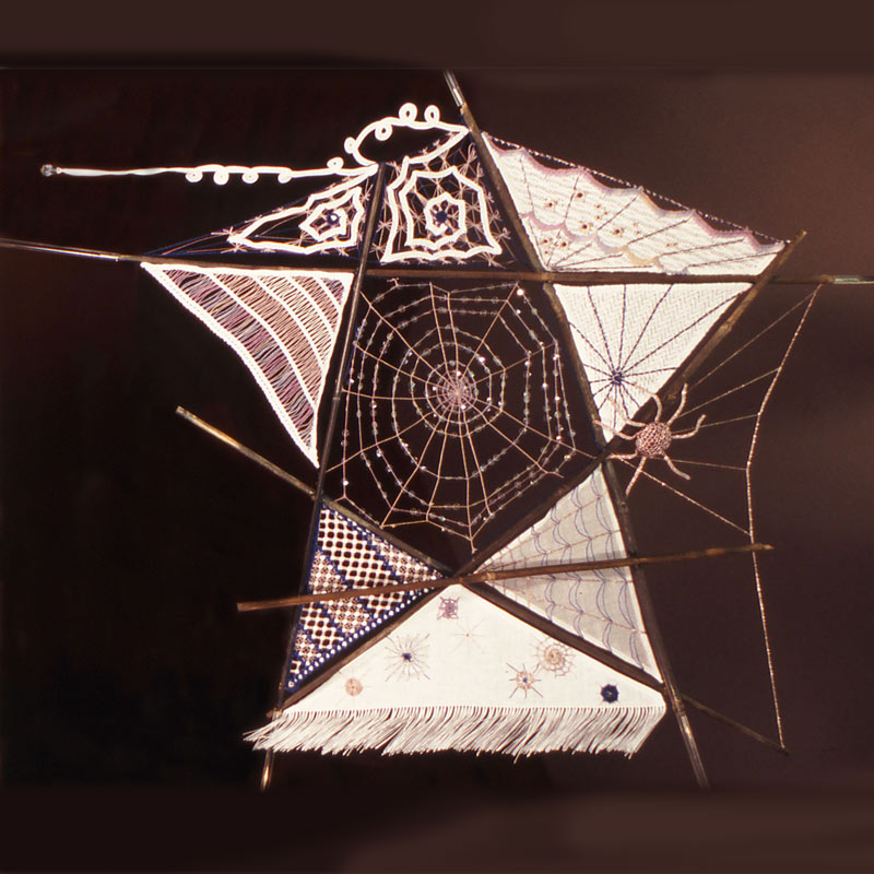 Photo of a star-shaped embroidery of a spider's web with various embroidery pieces filling some of the shapes, and extending beyond the star.