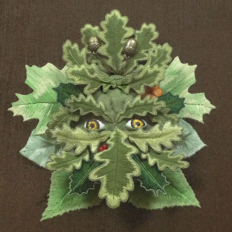A photo of a dimensional embroidery with pieces layered forming a face with leaves and eyes.