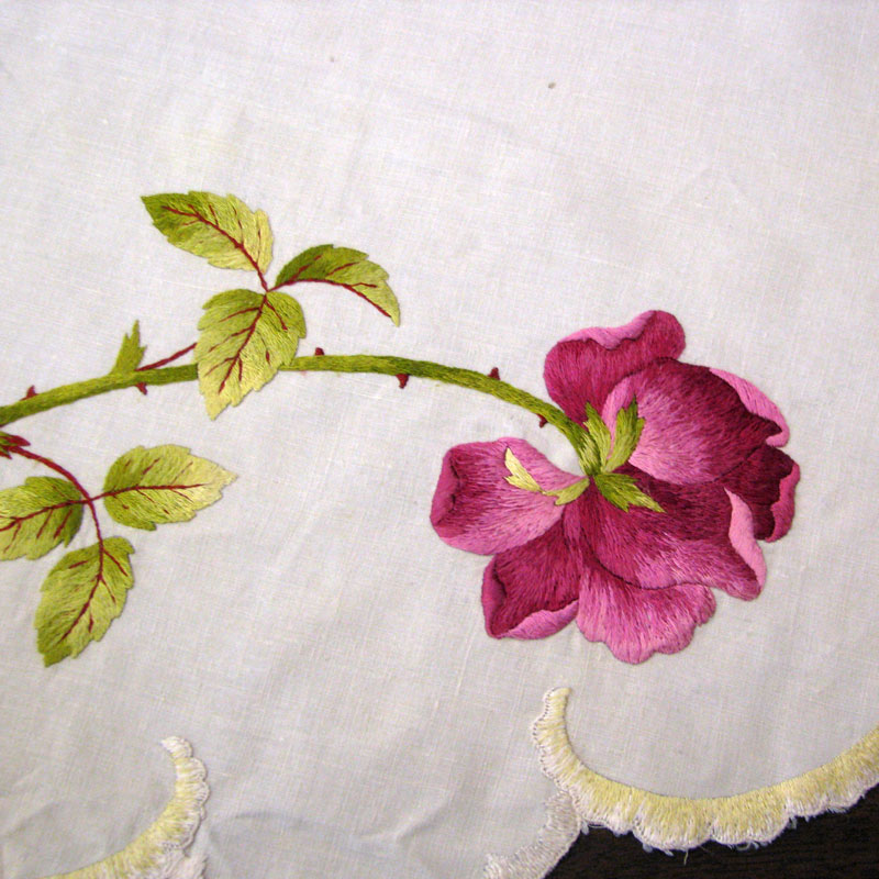 Close up photo of an rose near the edge of a tablecloth.