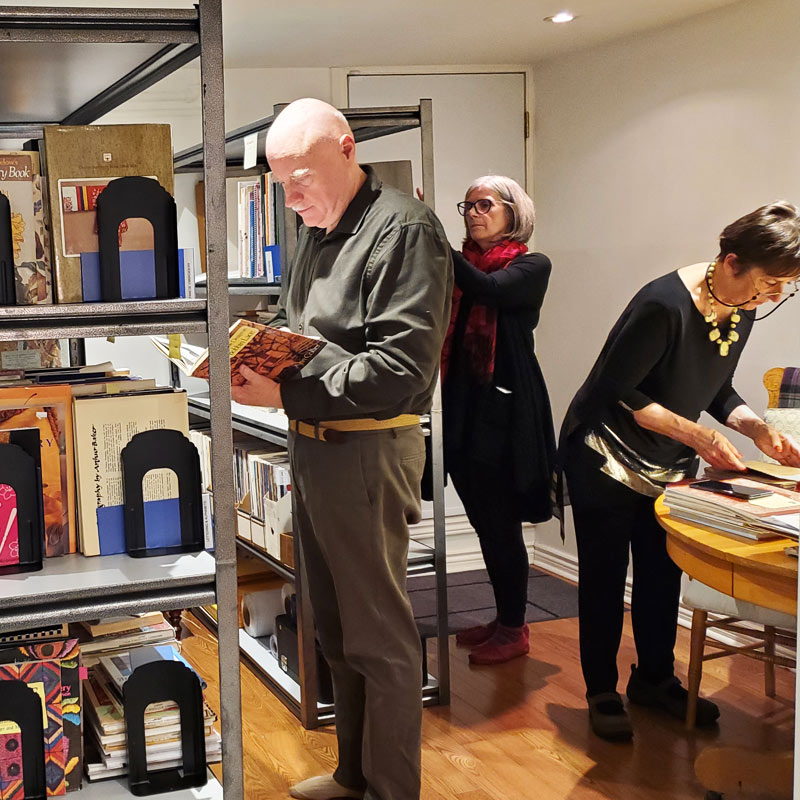 Photo of three people handing books, one is putting some on a shelf, the others are checking publication information inside the books.