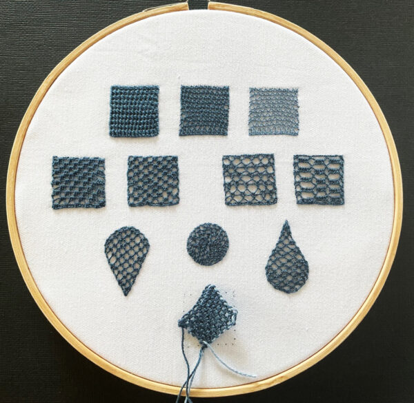 A photo showing examples of dark blue needlelace filling stitches in sqaure, teardrop and circular shapes in an embroidery hoop.