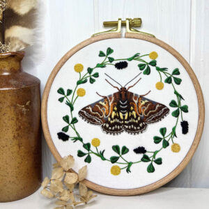 Photo of an embroidered moth and a flower garland in a round hoop sitting on a counter.
