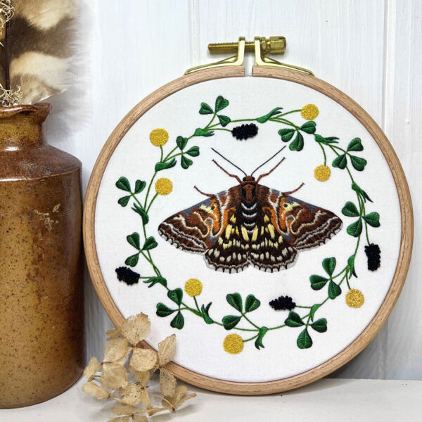Photo of an embroidered moth and a flower garland in a round hoop sitting on a counter.
