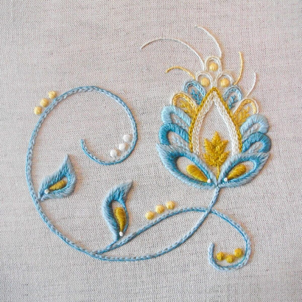 Photo of an embroidery of a swirled fantasy flower, stem and leaves in the Jacobean style stitched with blues and yellows.