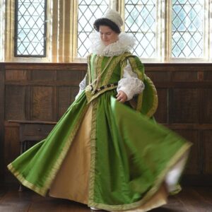 Photo of a woman in an historic-style full length dress in green with an embroidered bodice, a gold underskirt and gold trim. There are full puffy sleeves and a neck ruff.