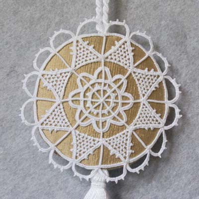 Close up photo of a round ornament with a lacy star over gold fabric and with a scalloped edge in lace.