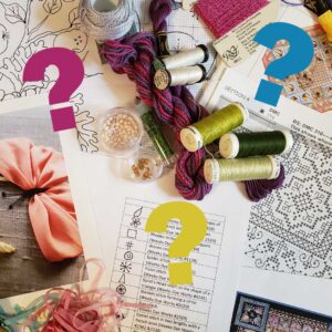 Photo of embroidery charts, supplies and tools with colourful question marks scattered over but not obscuring the iamge.