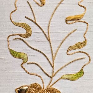 A photo of an embroidery of an oak leaf and two acorns stitched with metal and cotton threads.