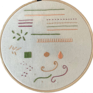 An off-white fabric showing various surface embroidery stitches and techniques. The stitches are dones in green, peach and dark red.