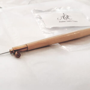 Wooden and brass Tambour beading hook with beading needle on end. Hooks is on a piece of plastic with the label ASC - Atelier Saint Clare.