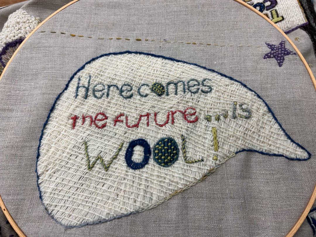 Part of Kathleen's canvas, this one says "Here comes the future...is Wool!". The words are stitched in various types and colours of yarn, and the words are on a background of off-white stitching.