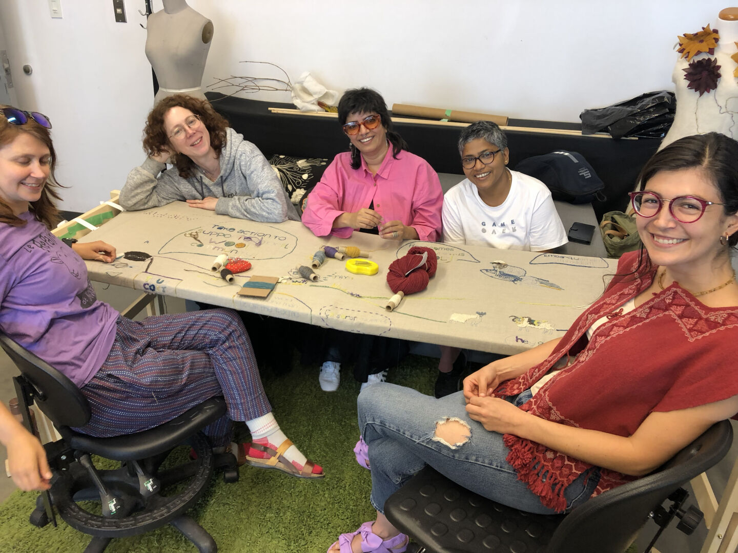 Several ladies sitting around a frame on which the canvas is stretched. They are working on various images with different shades and types of wool.